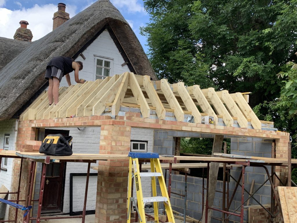 Brick and timber extension in progress, man drilling on roof. Attached to white brick thatched house,KL and Sons Building Services, Devizes, Marlborough, Calne, Bath