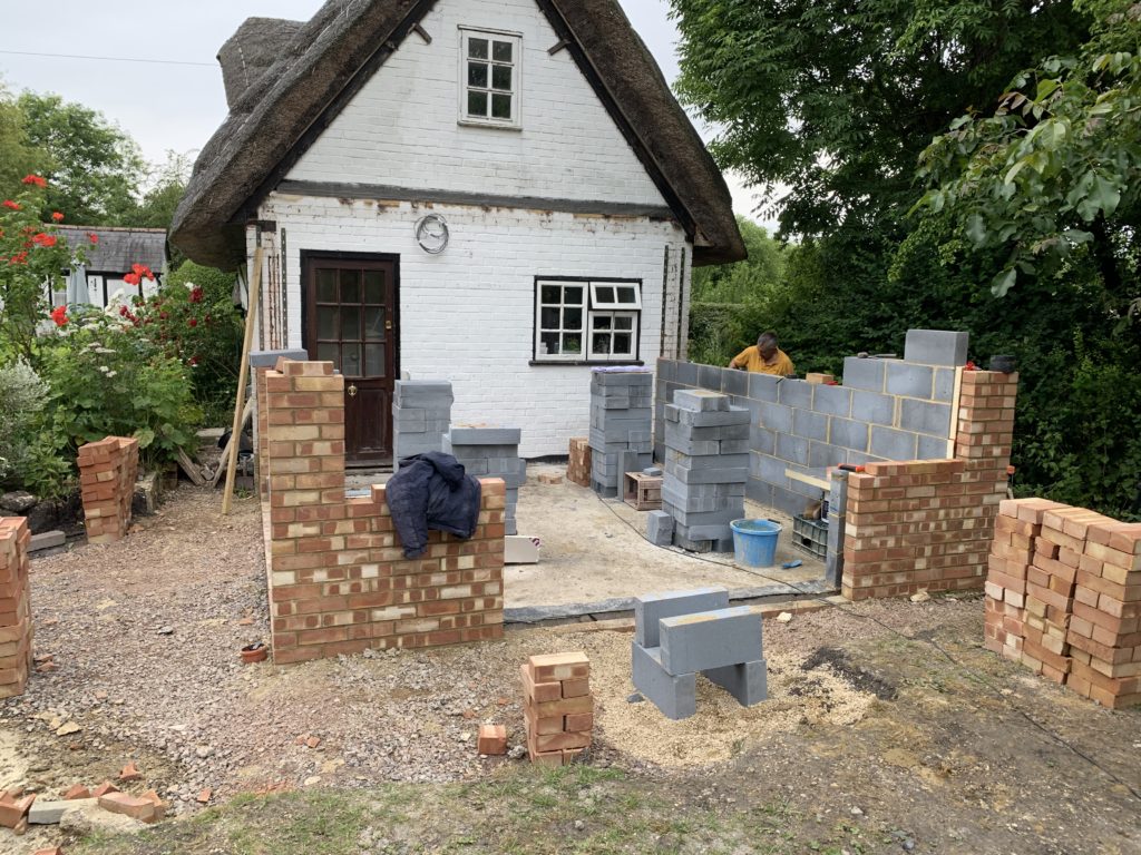 Brick extension in progress, man building grey brick wall. Attached to white brick thatched house,KL and Sons Building Services, Devizes, Marlborough, Calne, Bath